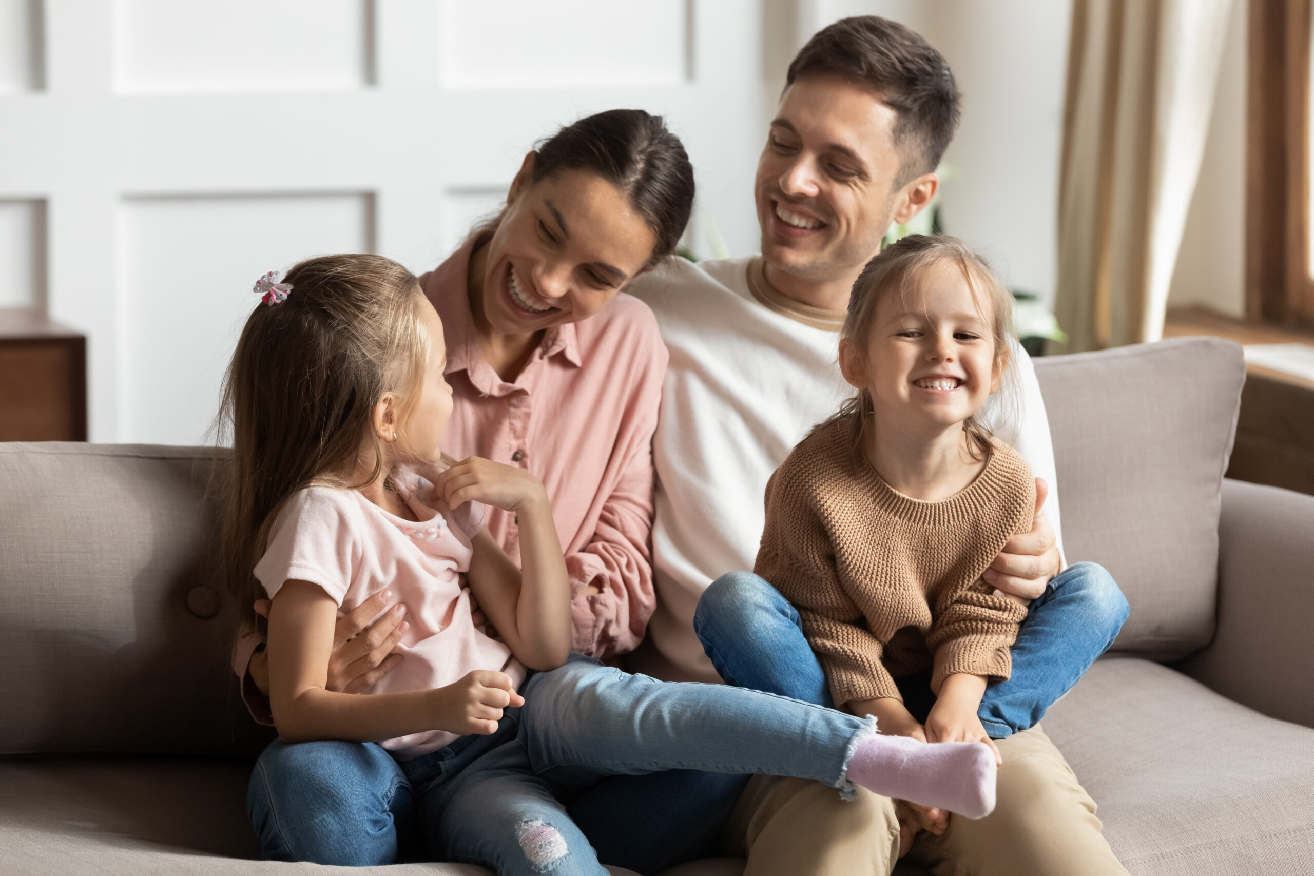 Happy family of four sitting on a sofa and smiling at each other