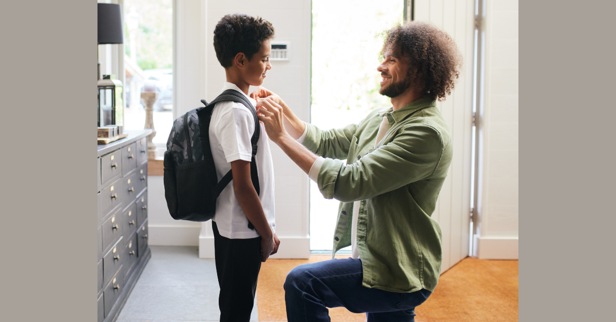 Image of father kneeling down in front of his son and doing up his school tie, illustrating family-friendly working for an education session